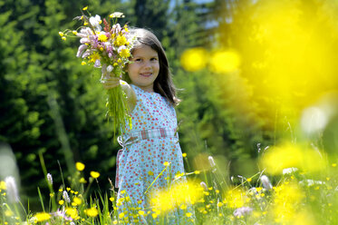 Girl (6-7) holding bunch of flowers in meadow, smiling - WESTF01409
