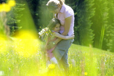 Mother and daughter (6-7) hugging in meadow, side view - WESTF01391