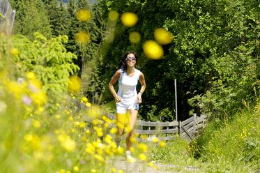 Junge Frau joggt auf einer Wiese, lächelnd - WESTF01440