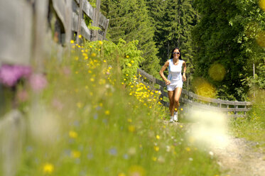 Junge Frau joggt auf einer Wiese, lächelnd - WESTF01438