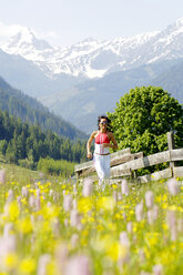Junge Frau joggt auf einer Wiese, lächelnd - WESTF01430
