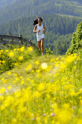 Junge Frau joggt auf einer Wiese, lächelnd - WESTF01424