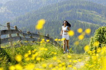 Junge Frau joggt auf einer Wiese, lächelnd - WESTF01421