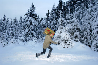 Junger Mann trägt Weihnachtsgeschenk im Schnee, Seitenansicht - HHF00456