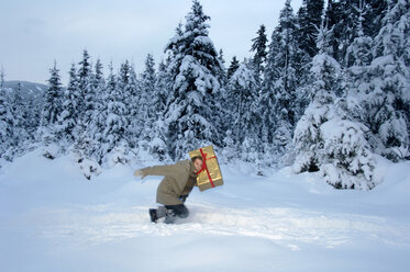 Junger Mann trägt Weihnachtsgeschenk im Schnee, Seitenansicht - HHF00455