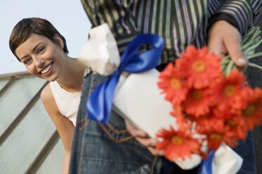 Man hiding present and flowers while woman looking - WEST01533