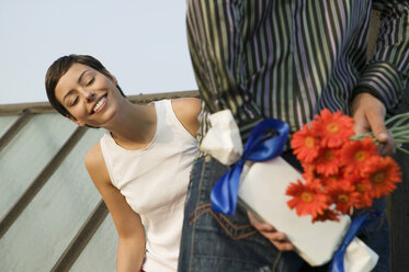 Man hiding present and flowers while woman looking - WEST01532