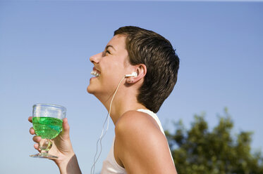 Junge Frau hört MP3-Player mit Glas in der Hand, lächelnd, Seitenansicht - WEST01476