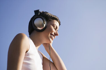 Young woman listening to music, smiling, low angle view - WEST01467