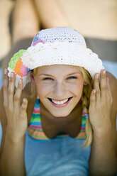 Young woman wearing sunhat lying on beach, smiling, portrait - WESTF01857