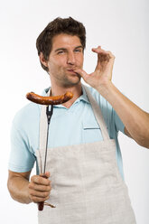 Young man with grilled sausage on fork, portrait - WESTF01650