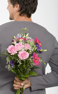 Junger Mann hält einen Blumenstrauß hinter dem Rücken, lächelnd, Nahaufnahme - WESTF01606