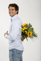 Junger Mann hält einen Blumenstrauß hinter dem Rücken, lächelnd, Nahaufnahme, Porträt - WESTF01600
