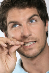 Young man holding toothpick between teeth, close-up - WESTF01570