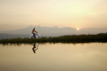 Österreich, Alpen, Frau fährt Fahrrad am See, Seitenansicht - HHF00586