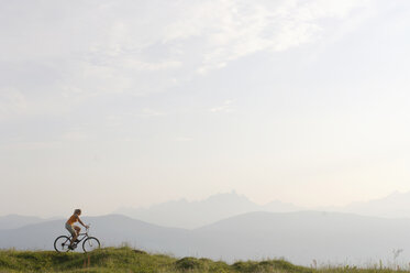 Austria, woman riding bicycle on meadow - HHF00568