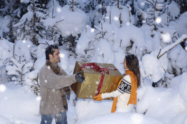 Junges Paar hält Geschenk im Schnee - HHF00561