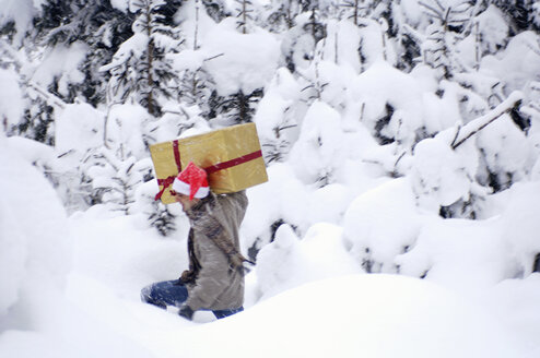 Junger Mann geht im Schnee und trägt ein Geschenk - HHF00558