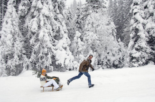 Man pulling sledge with woman holding Christmas tree - HHF00541