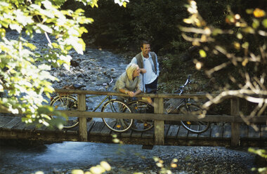 Paar mit Fahrrädern, stehend auf Holzbrücke, lächelnd - HHF00448