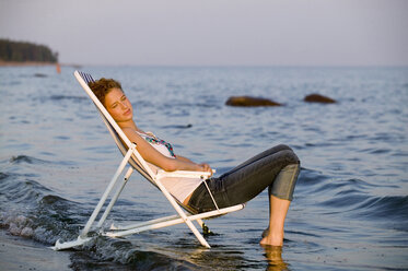 Young woman resting in deck chair on beach, side view - WESTF01796