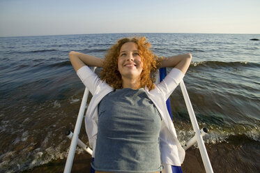 Young woman relaxing in deck chair on beach, smiling, close-up - WESTF01775