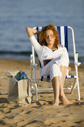 Junge Frau sitzt im Liegestuhl am Strand und liest ein Buch - WESTF01769