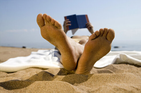 Frau liegt am Strand und liest ein Buch (Fokus auf den Vordergrund) - WESTF01752