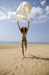 Junge Frau läuft am Strand, hält Badetuch - WESTF01733