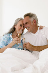 Mature couple on bed toasting champagne, smiling - WESTF01951