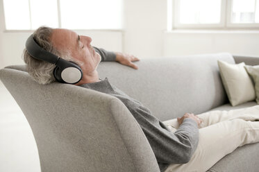 Mature man sitting on sofa, listening music, eyes closed - WESTF01945