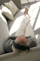 Mature man wearing headphones, sitting on sofa, overhead view - WESTF01944