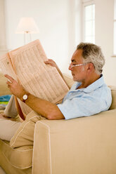 Älterer Mann liest Zeitung auf Sofa, Seitenansicht, Nahaufnahme - WESTF01912