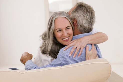 Mature couple embracing on sofa, smiling - WESTF01889