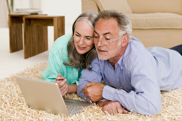 Älteres Paar im Wohnzimmer, auf dem Boden liegend mit Laptop - WESTF01880
