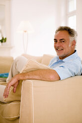 Mature man sitting on sofa in living room, portrait, close-up - WESTF01863