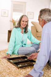 Älteres Paar spielt Backgammon im Wohnzimmer, lächelnd - WESTF01860