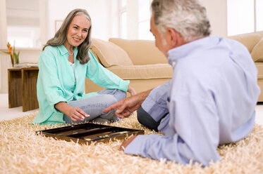 Älteres Paar spielt Backgammon im Wohnzimmer, lächelnd - WESTF01859