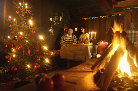 Paar sitzt am Tisch in einer Berghütte und betrachtet den Weihnachtsbaum, lizenzfreies Stockfoto