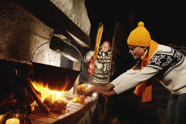 Mid adult couple in alpine hut, woman warming hands at fireplace - HHF00747