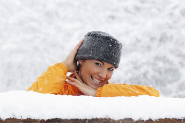 Junge Frau im Schnee, an ein Holzgeländer gelehnt - HHF00684
