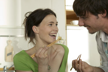 Young couple eating with chopsticks, smiling - WESTF02194