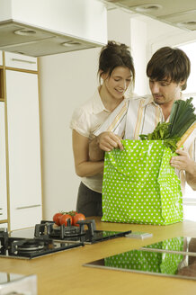 Junges Paar in der Küche, schaut in die Einkaufstasche - WESTF02118