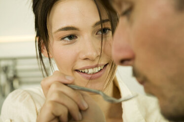 Young couple in kitchen, woman feeding man - WESTF02104