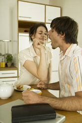 Young couple in kitchen, woman feeding man - WESTF02102