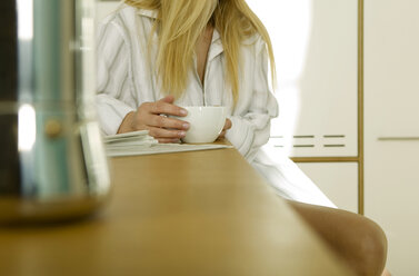 Junge Frau sitzt in der Küche mit einer Tasse Kaffee, Mittelteil - WESTF02097