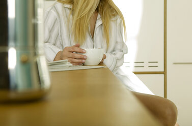 Young woman sitting in kitchen with cup of coffee, mid section - WESTF02097