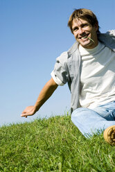 Mid adult man sitting in park biting grass, smiling, low angle view - WESTF02251