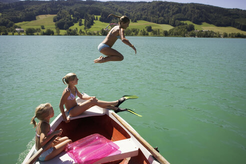 Mädchen (8-15) sitzen auf einem Boot, eine springt ins Wasser, Seitenansicht - WESTF01709