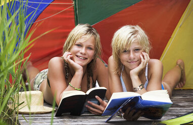 Teenager-Mädchen (13-15) unter Sonnenschirm auf Steg liegend, Buch lesend, Porträt - WESTF01698
